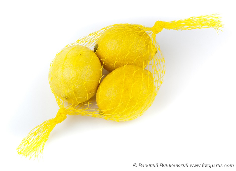 Citrus_limon_2010_0202_1609.jpg - Three yellow Lemons in a string-bag on a white background.